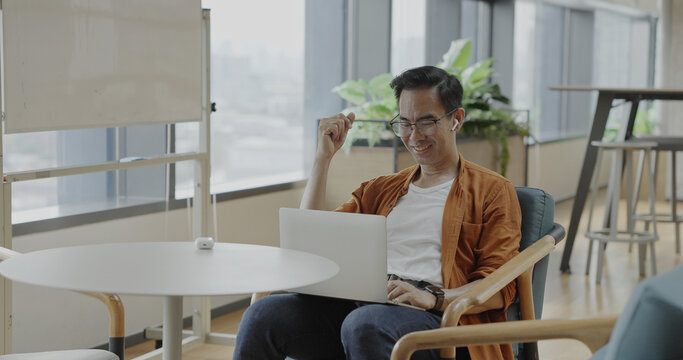 Senior Asian businessman wearing headset celebrates success during online meeting in modern co-working space. Remote work and business communication concept	