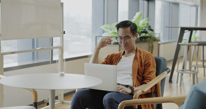 Senior Asian businessman wearing headset celebrates success during online meeting in modern co-working space. Remote work and business communication concept	