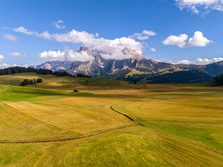 Aerial view over meadows in front of Alpe di Siusi peaks, in Dolomites, Italy. Beautiful hut on alpine plateau Seiser Alm. Wooden cabins in south Tyrol. Dolomites UNESCO World Heritage.