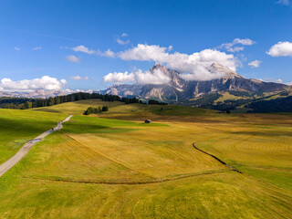 Aerial view over meadows in front of Alpe di Siusi peaks, in Dolomites, Italy. Beautiful hut on alpine plateau Seiser Alm. Wooden cabins in south Tyrol. Dolomites UNESCO World Heritage.