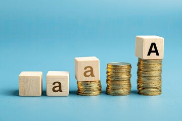 Image showing alphabet blocks, letters "a" and "A", atop stacks of coins, on blue backdrop