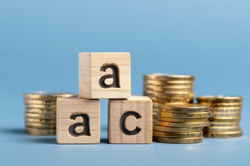 Three wooden letter blocks stacked and piles of gold coins against a vibrant blue backdrop