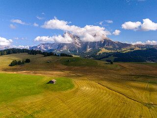 Aerial view over meadows in front of Alpe di Siusi peaks, in Dolomites, Italy. Beautiful hut on alpine plateau Seiser Alm. Wooden cabins in south Tyrol. Dolomites UNESCO World Heritage.