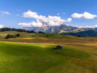 Aerial view over meadows in front of Alpe di Siusi peaks, in Dolomites, Italy. Beautiful hut on alpine plateau Seiser Alm. Wooden cabins in south Tyrol. Dolomites UNESCO World Heritage.