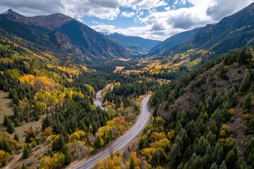 Aerial perspective of a mountain valley landscape showcasing a winding road amid autumn foliage