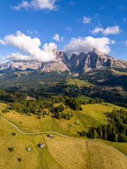 Aerial view over meadows in front of Alpe di Siusi peaks, in Dolomites, Italy. Beautiful hut on alpine plateau Seiser Alm. Wooden cabins in south Tyrol. Dolomites UNESCO World Heritage.