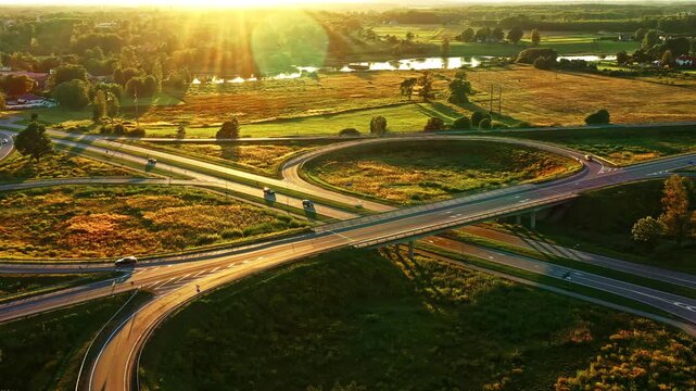 Vehicles Driving Through Cloverleaf Intersection at Sunset Golden Sunlight in Latvian Countryside.