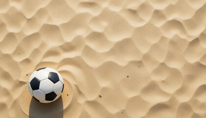 A classic black and white soccer ball on golden beach sand with bright sunlight