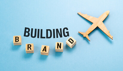 A wooden airplane is flying over a blue background with the letters Building Brand