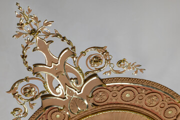 A decorative gold and pink ornamental piece featuring scrolling vines and leaves