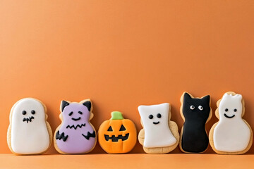 Cute Halloween cookies in the shapes of ghosts, pumpkins, cats , arranged on a pastel orange background with ample negative space