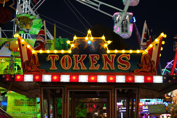 Illuminated tokens sign and Ferris wheel at the vibrant Goose Fair in Nottingham, England, on a festive evening.