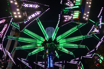 Vibrant fairground ride with dazzling green and purple lights spinning at night during Goose Fair in Nottingham, England.