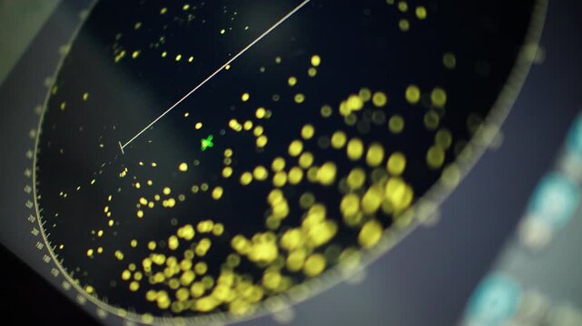 Close-up of a rotating radar screen with a sweeping line and yellow blips marking detected targets, centered on a green marker, showing real-time tracking on a circular interface