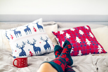 Feet in woollen socks in Christmas holidays. Woman relaxed on bed with coffee cup. Close up on feet. Winter and Christmas holidays concept.