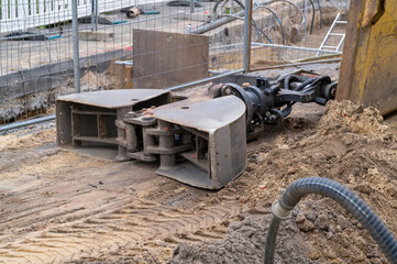 Excavator hydraulic grab attachment lying on ground at construction site