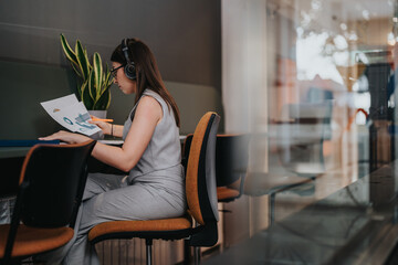 Business associate wearing headphones studies printed charts at a workstation in a modern office. The photo showcases a focus on analysis, productivity, and concentration in a working setting.