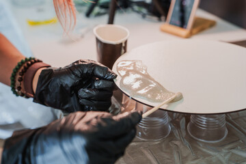 Epoxy resin ocean art creation process. Artisan pouring and spreading epoxy resin with pigments to create an abstract beach with ocean waves on a round panel.