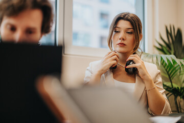 A businesswoman holding headphones in a modern office environment, appearing thoughtful and professional. The atmosphere conveys a productive work setting with attention to detail.