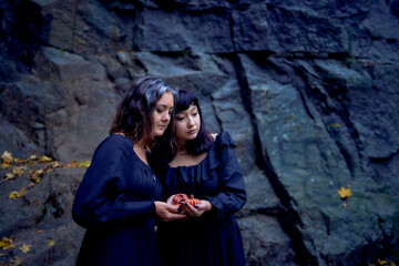 two women in the  black long dresses near black rocks on Halloween with candles in the form of...