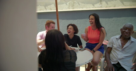 Diverse group of friends laughing and enjoying conversation at an outdoor gathering, seated around...