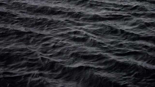 Dark, choppy ocean surface with subtle ripples and textured waves under overcast light, capturing a moody, minimalist seascape with rolling motion and shadows across restless water