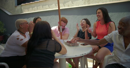 Diverse group of friends and family cheerfully raising cups in unison, toasting together at an...