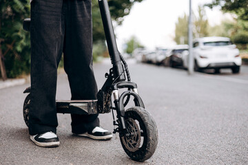 Close-up of an electric scooter wheel with a teenage boy riding on a street.