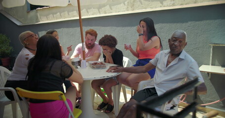 Diverse group of friends and family cheerfully raising cups in unison, toasting together at an...