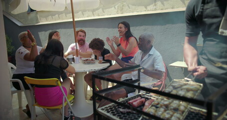 Man grilling food on barbecue while diverse group of friends and family claps and celebrates his cooking, bonding and laughing together at joyful backyard gathering