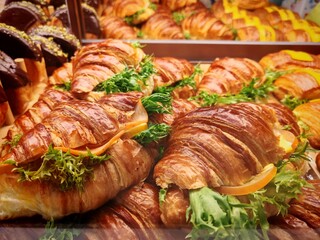Golden, flaky croissants filled with crisp green lettuce and slices of cheese, displayed in a bakery showcase. The vibrant layers and glossy pastry surface highlight freshness and appetizing appeal. 