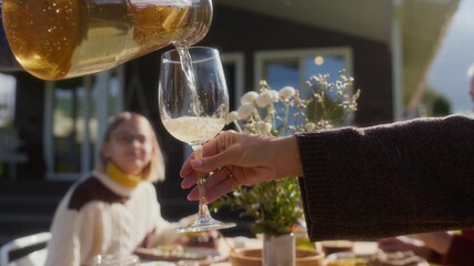Cropped slowmo shot of hands pouring delicious homemade lemonade into glass at festive table outdoors during warm family gathering on sunny fall day - Powered by Adobe