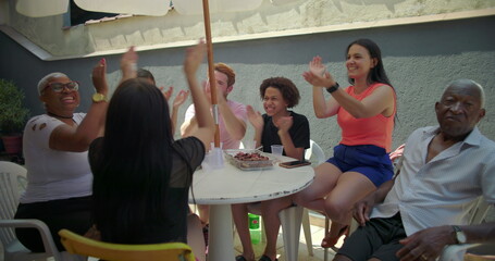 Diverse group of friends and family clapping and laughing in joyful celebration during outdoor...