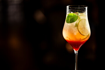 Layered cocktail or mocktail in a wine glass with red and yellow tones, garnished with lime and mint, isolated on dark background. Elegant, refreshing, and visually striking.