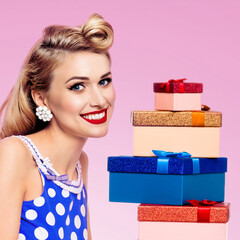 Big sale, price discounts ad concept - happy expressive smile blond hair beautiful cute woman pin up style dress. Pinup girl with stack of colorful gift boxes, isolated pink background. Square image