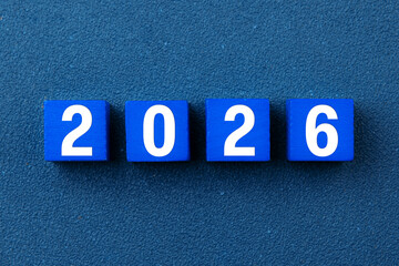 2026 Happy New Year. Wooden cube block 2026 greeting card on blue. Concept 2026 New Year background. Business, resolutions, goals, inspiration, success, ideas