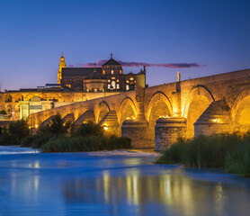 Obraz premium An old Roman bridge and the Moorish Mezquita at sunset in Cordoba, Spain. The bridge was built in the first century BC and straddles the Guadalquivir River.