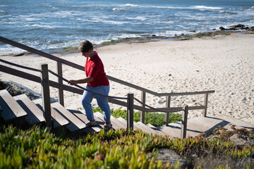 Middle-aged woman sitting on a wall looking at the ocean in Portugal, enjoying a sunny summer day