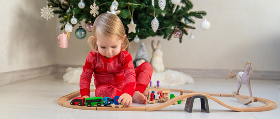 Child in Pajamas Playing with a Wooden Train Set under the Christmas Tree