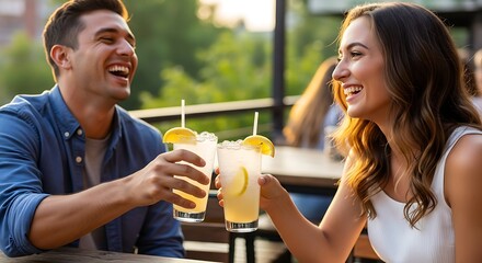 Happy young couple laughing and toasting with cocktails on a sunny outdoor patio.