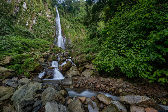View of the cascading Benowo Waterfall plunges amidst verdant foliage and moss-covered rocks, creating a serene and picturesque scene, Ungaran, Central Java, Indonesia.