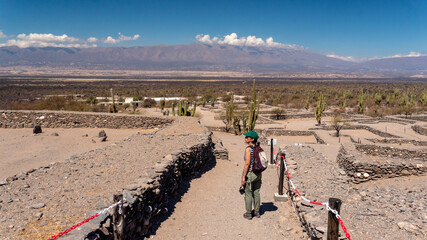 Young woman walking within the Quilmes tribe ruins located in a desert valley surrounded by large hills in Tucuman, Argentina