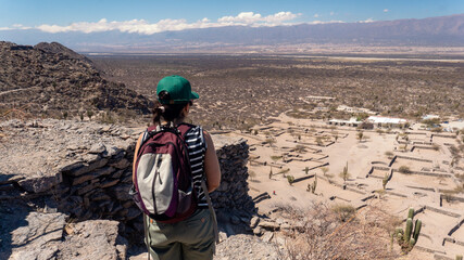 Young woman walking within the Quilmes tribe ruins located in a desert valley surrounded by large hills in Tucuman, Argentina