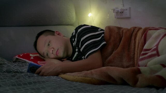 Before going to bed, the boy stayed up late playing on his phone and watching short videos. People nowadays are addicted to using their phones, laughing foolishly while watching videos. Excessive phon