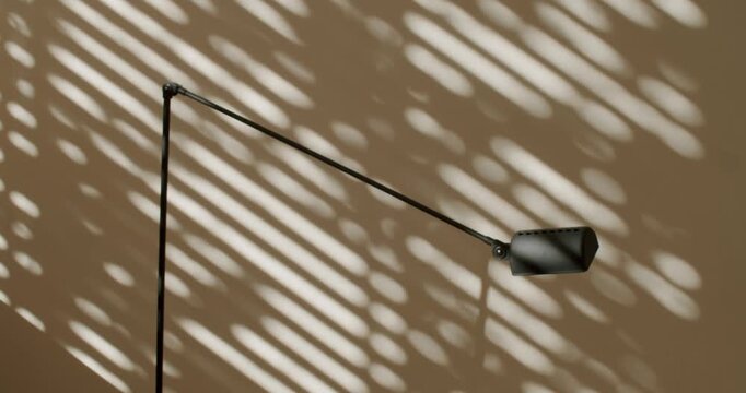 Sunlight streams through window blinds, casting dynamic shadows on a beige wall and a stylish black floor lamp. modern ambiance. Ideal for home decor, interior design,