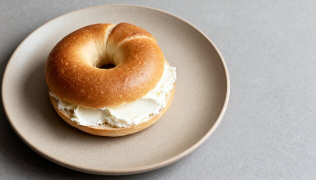 Golden bagel with a thick layer of cream cheese on a ceramic plate&mdash;simple, cozy breakfast in soft natural light.
