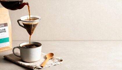 Cold brew pours over ice in a clear glass on a light wood table, with a coffee bag, cup and spoon—clean, refreshing café vibe.
