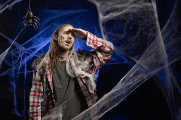 Creepy scary zombie man with ugly makeup looking far away distant touch forehead standing on spooky...