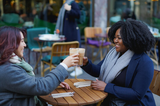Happy multiracial women cheering with coffee at bar terrace during winter time - Young people, lifestyle and diverse friendship concept