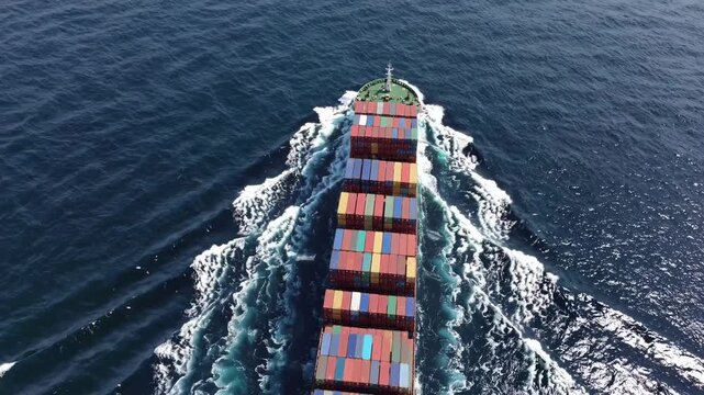 Aerial view of a cargo ship cutting through the ocean, showcasing vibrant containers. The video captures dynamic movement from a top-down angle.